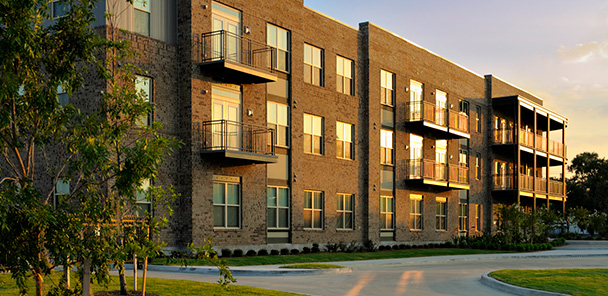 40-unit corridor building at sunset with metal balconies, dark red brick, and driveways.